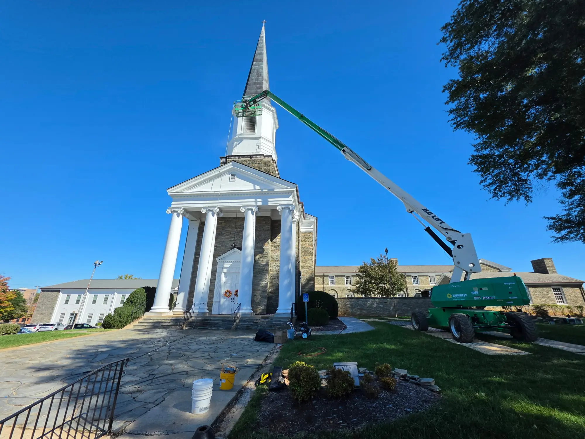 White-painted church columns, entry trim, and steeple contrast with tan stone walls beneath a gray spire