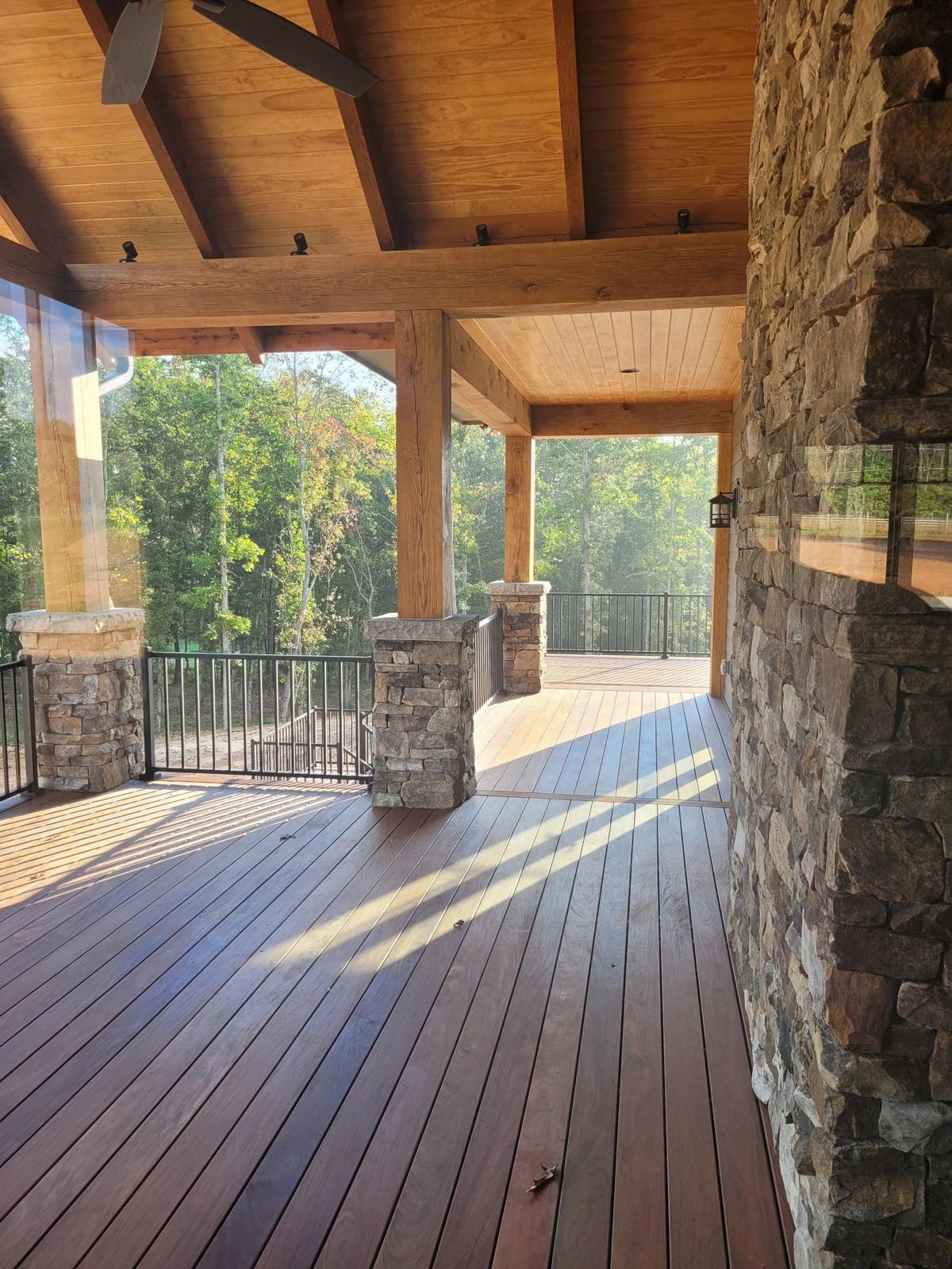Covered porch with a stained wood ceiling and beams, stone columns and a stone fireplace