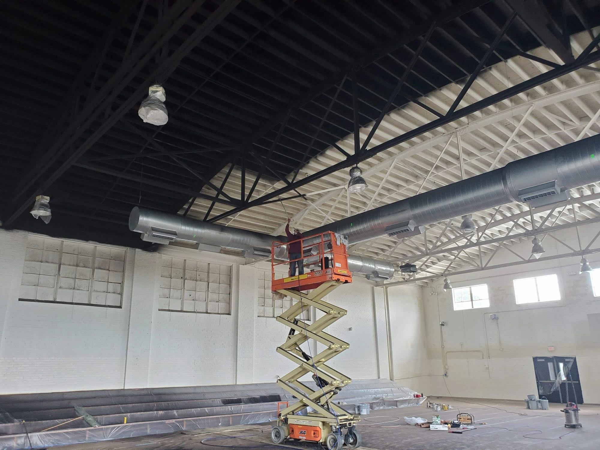 Painter on a scissor lift painting a gymnasium ceiling black