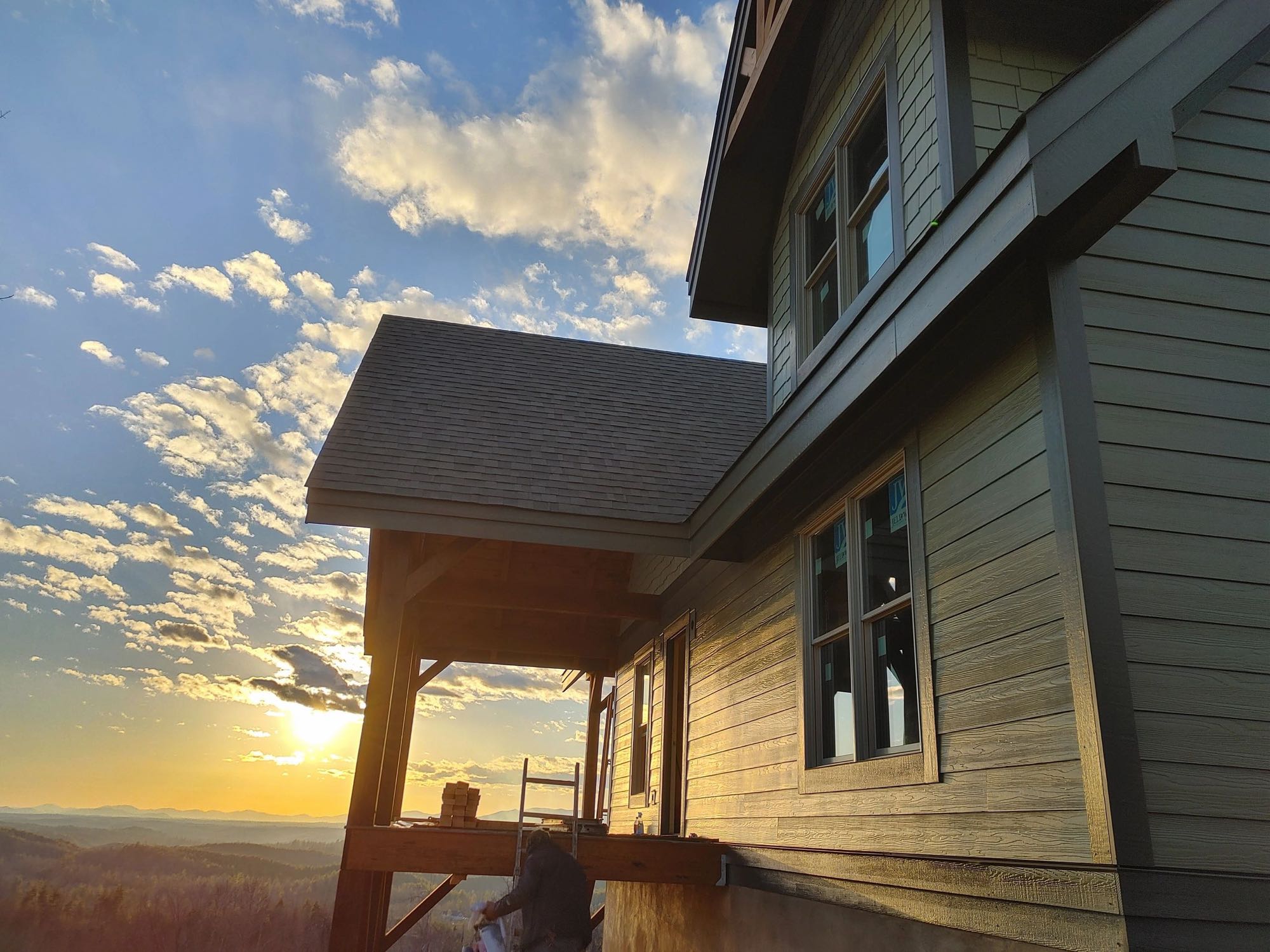 Mountain home with gray lap siding and a stained covered porch at sunset
