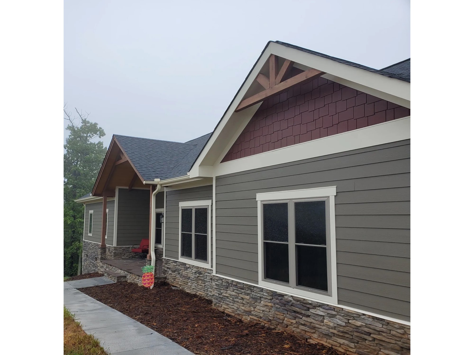 Ranch home with gray siding, a red shake gable, white trim and a stone base
