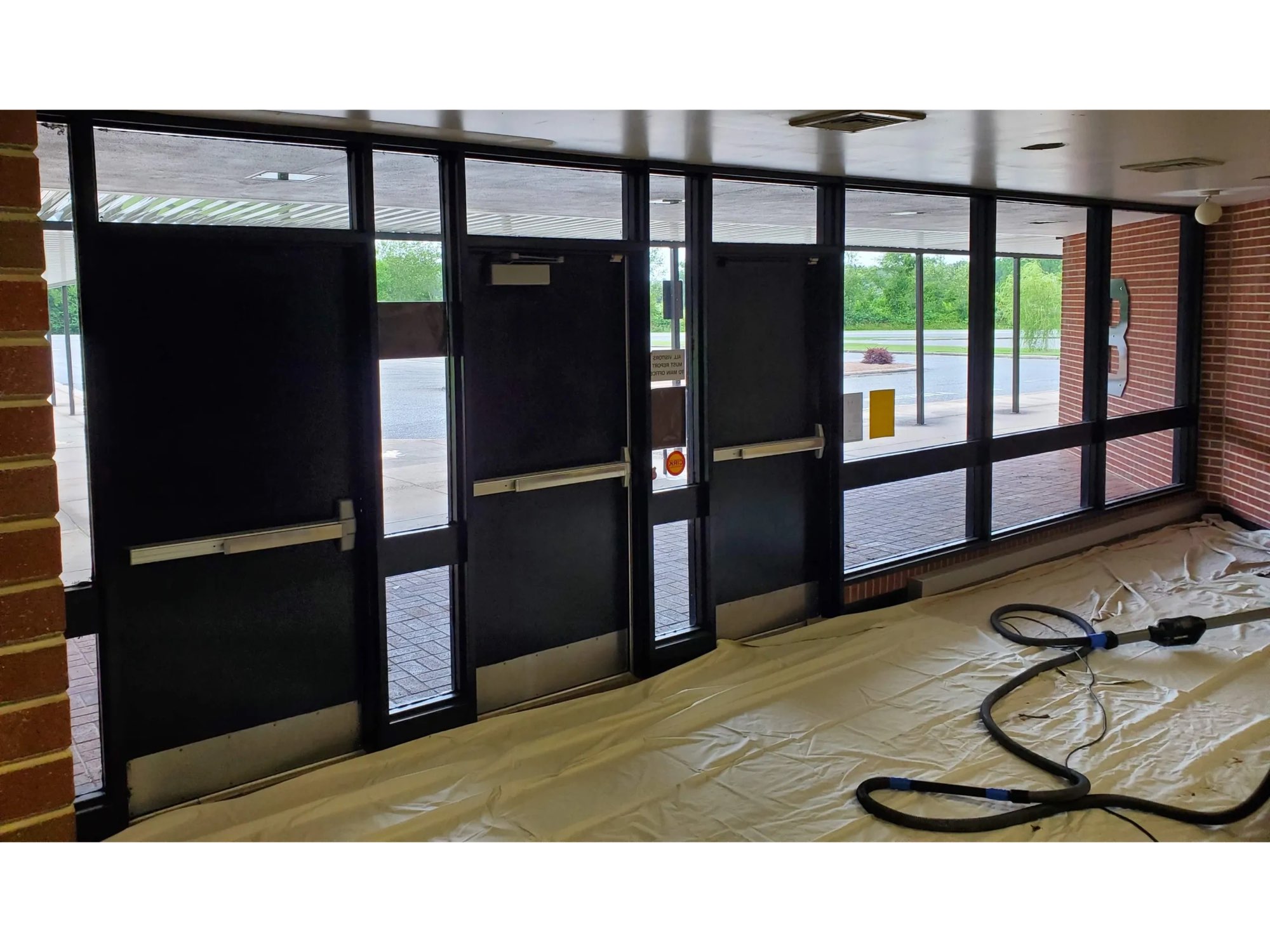 School entrance doors and window frames painted dark bronze, with drop cloths on the floor
