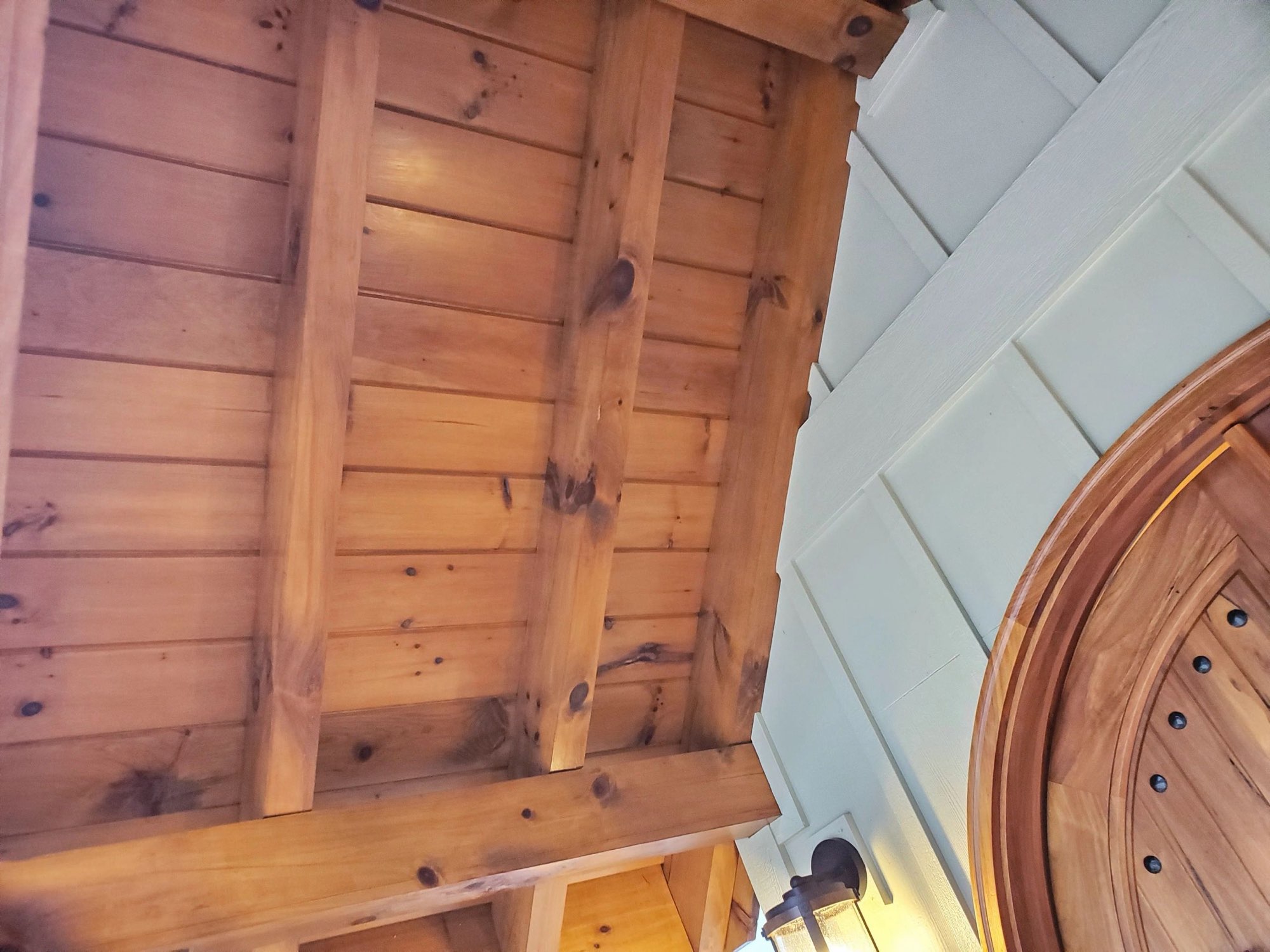 Stained pine porch ceiling with beams above an arched wooden door